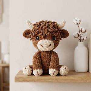 Pode incluir: Um peluche de vaca highland feito de fio castanho escuro e creme. O brinquedo apresenta uma textura felpuda e encaracolada, dois chifres de cor clara, olhos pretos grandes e um focinho creme arredondado, sentado numa posi&ccedil;&atilde;o sentada numa prateleira.
