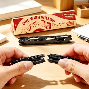 May include: A black, hollow, wishbone-shaped object being pulled apart into two pieces. Behind it sits a triangular cardboard box labeled ONE WISH WILLOW with illustrations of two people, the word CRACK, and the text AMAZE YOUR FRIENDS!