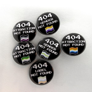 May include: Six circular black pin-back buttons featuring pixelated white text. Three buttons read 404 ATTRACTION NOT FOUND with small flags, two read 404 GENDER NOT FOUND with flags, and one reads 404 LABEL NOT FOUND with a flag at the bottom.