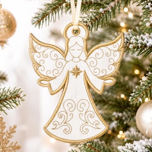 May include: A white fabric angel ornament featuring gold embroidered scrollwork patterns on the wings and dress. The angel has a closed-eye expression, a gold star at the center of the chest, and a gold halo, suspended by a thin cream ribbon.