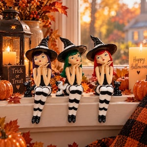 May include: Three witch figurines with black pointed hats, black tops, and black and white striped stockings. Each figure has a different hair color: purple, green, and red. They are posed with hands near their faces, sitting on a ledge.