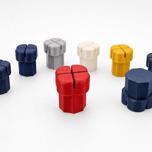 May include: A collection of eight small, cylindrical plastic objects with a cross-shaped slot on the top surface. The items are colored in red, yellow, white, silver, and various shades of blue, featuring a ridged, multi-sided vertical base.