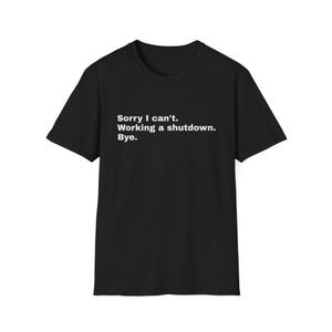 Peut inclure: Un t-shirt noir à manches courtes avec un texte blanc imprimé sur la poitrine qui dit : Sorry I can't. Working a shutdown. Bye. Le vêtement possède une encolure ronde et une coupe standard, offrant un fond noir uni pour le texte.