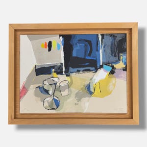 May include: An abstract print in a light wood frame featuring a still life composition with a yellow vessel, a white cup, and a dark blue form. The artwork uses bold blocks of color including black, blue, yellow, and pink against a neutral background.
