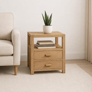 May include: A light oak wood nightstand featuring two drawers with horizontal wooden pulls and an open shelf above. A white ceramic pot containing a green snake plant sits on the top surface, and two stacked books rest on the open shelf.