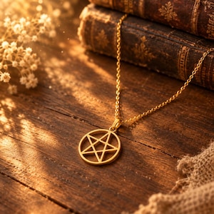 Può includere: Una collana color oro con un ciondolo circolare caratterizzato da un design ritagliato a stella a cinque punte. Il ciondolo è fissato a una delicata catenina color oro, che mostra una finitura metallica lucida che riflette la luce calda.