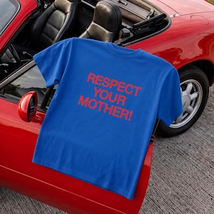 May include: A bright blue short-sleeved t-shirt featuring the text "RESPECT YOUR MOTHER!" printed in bold red capital letters across the chest. The garment has a classic crew neckline and a straight hem, showcasing a simple and clean design.