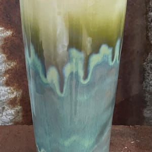 May include: A handmade ceramic tumbler with a distinctive glaze. The top is a pale yellow-green, transitioning to a darker green, and then to a teal blue at the bottom. The base is white.