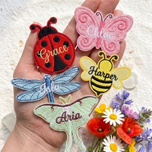 May include: Five embroidered insect and butterfly patches featuring names: a red ladybug labeled Grace, a pink butterfly labeled Chloe, a yellow bee labeled Harper, a blue dragonfly labeled Isla, and a light green moth labeled Aria.