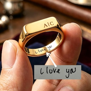 Peut inclure: Une bague chevalière dorée présentant les lettres gravées "AIC" sur la surface supérieure et l'inscription manuscrite "I love you" gravée sur l'anneau intérieur, accompagnée d'une référence visuelle du style d'écriture.