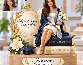 May include: A custom figurine of a graduate wearing a navy gown and cap, sitting on a stack of books labeled Dream and Achieve. Beside them is an open book with the text The next chapter begins with you, a bouquet, and a base reading Jasmine Class of 2026.