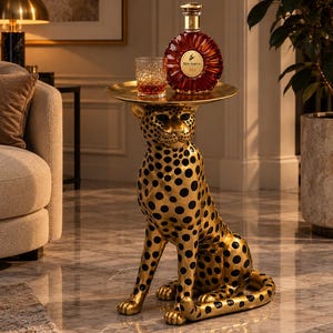 Puede incluir: Una mesa auxiliar dorada con forma de leopardo sentado con manchas negras. La mesa cuenta con una bandeja circular plana de color dorado en la parte superior que sostiene un decantador de cristal de coñac Remy Martin XO y un vaso a juego.