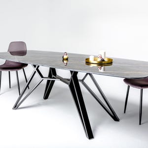 May include: A dining table with a dark gray marble-patterned top and a black geometric metal base. Two dark purple upholstered chairs with black metal legs are positioned at the table. A gold tray holds two white candles and a small bird figurine.