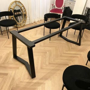 Può includere: Un telaio per tavolo rettangolare in metallo nero con quattro gambe angolate collegate da barre di supporto orizzontali. La struttura è realizzata in tubi quadrati cavi con finitura opaca e fori di montaggio preforati sui binari.