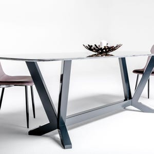 Op de afbeelding: Een rechthoekige eettafel met een wit marmeren blad en een donkergrijs metalen frame met schuine poten. Een donkerbruine decoratieve schaal met een witte kaars staat op de tafel, geflankeerd door twee stoelen met mauve gestoffeerde zittingen.