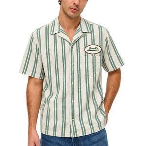 Peut inclure: Une chemise à manches courtes boutonnée avec un motif à rayures verticales crème et vert foncé. La chemise présente un col cubain, une poche poitrine unique et un écusson ovale sur la poitrine gauche avec le texte Cassell's en rouge foncé.
