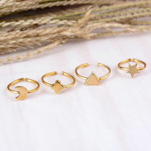 Könnte beinhalten: Ein Set aus vier goldfarbenen Ringen mit verschiedenen offenen Ringdesigns. Die Ringe zeigen eine Mondsichel, eine vierblättrige Kleeblattform, ein ausgefülltes Dreieck und einen fünfzackigen Stern. Jeder Ring hat eine dünne, polierte Metallschiene.