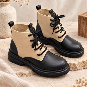 Könnte beinhalten: Ein Paar Stiefeletten im zweifarbigen Design mit beigen Seitenteilen sowie schwarzem, lederartigem Material an Zehenkappe, Ferse und Sohle. Die Stiefel haben schwarze Schnürsenkel, eine abgerundete Spitze, eine dicke Profilsohle und eine Zugschlaufe.
