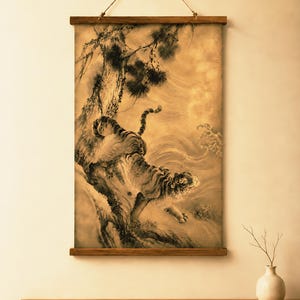 May include: A vertical wall hanging featuring a sepia-toned ink wash painting of a tiger climbing a pine tree. The artwork is mounted between two horizontal wooden bars at the top and bottom, suspended by a thin cord attached to the upper bar.