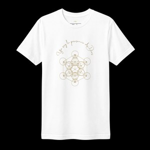 Puede incluir: Una camiseta blanca de manga corta con un diseño geométrico dorado del Cubo de Metatrón centrado en el pecho. Sobre el gráfico, el texto "Yo soy la presencia de Dios" está impreso en una fuente cursiva fina de color dorado.