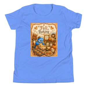 Op de afbeelding: Een lichtblauw t-shirt met een centrale afbeelding van een blauwe vogel met een koksmuts en schort die ingrediënten in een kom mengt. De tekst luidt Fall Baking, Grateful Thankful Blessed, Flour, Sugar en Pumpkin Spice, omringd door herfstbladeren.