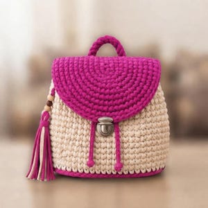 May include: A crochet backpack featuring a cream-colored body and a vibrant magenta flap. The bag includes a top handle, a metallic silver push-lock closure, and a decorative side tassel with wooden beads in shades of brown and cream.