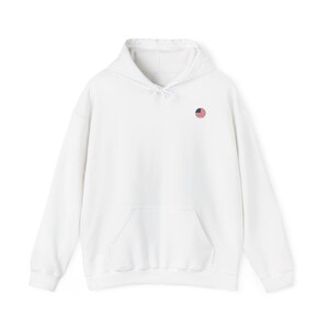 Peut inclure: Un sweat-shirt à capuche blanc à manches longues avec un petit écusson circulaire brodé sur la poitrine gauche. L'écusson représente les rayures et les étoiles rouges, blanches et bleues du drapeau des États-Unis. Il possède une poche kangourou.