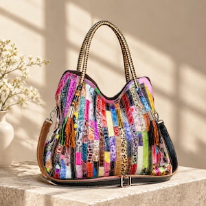 Op de afbeelding: Een veelkleurige patchwork handtas met verticale stroken in diverse texturen en patronen, waaronder dierenprints, metallic afwerkingen en levendige kleuren. De tas heeft twee gevlochten handvatten, twee decoratieve kwastjes en een afneembare schouderriem.