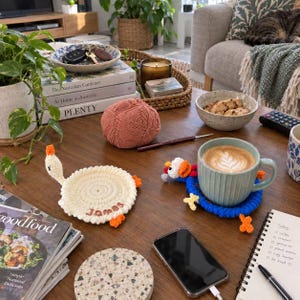 Peut inclure: Deux dessous de verre ronds au crochet en forme d'oie. L'un est crème avec le nom James brodé en marron, l'autre est bleu avec une tête et des pattes d'oie multicolores. Les deux présentent des pattes orange et une tête blanche avec un bec orange.