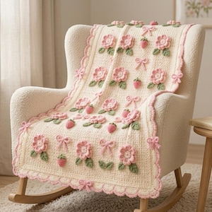 Può includere: Una coperta all'uncinetto color crema con fiori rosa tridimensionali, piccole fragole rosse e fiocchi rosa chiaro. La coperta presenta un bordo smerlato con finiture rosa ed è drappeggiata su una sedia a dondolo imbottita color crema.
