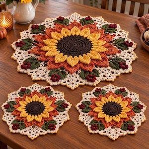Puede incluir: Un juego de tres tapetes redondos de ganchillo con un centro de girasol marrón oscuro, pétalos amarillos y naranjas, rodeados de hojas verdes y pequeñas bayas de color rojo oscuro, con un borde de encaje en color crema.