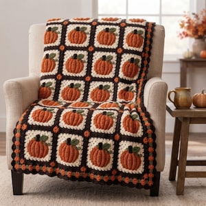 May include: A crochet blanket featuring a repeating pattern of orange pumpkins with green stems on cream-colored square patches, separated by dark brown borders. The blanket has a scalloped edge with small orange and green accents throughout.
