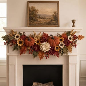 Op de afbeelding: Een decoratieve slinger met gehaakte herfstelementen, waaronder twee oranje pompoenen, diverse herfstkleurige bladeren in rood, oranje en groen, zonnebloemen, witte dahlia's en kleine rode bessen, gerangschikt in een horizontale compositie.