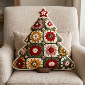 May include: A Christmas tree-shaped throw pillow constructed from crocheted granny squares in shades of red, green, yellow, and cream. The pillow features a star-shaped topper, small decorative bobbles along the edges, and a brown rectangular base.