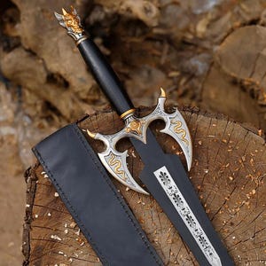 Op de afbeelding: Een zwarte dolk met een zilver- en goudkleurige stootplaat met slangengravures. Het handvat is zwart met een goudkleurige pommel in de vorm van een gehoornde schedel. Een zwarte schede ligt naast het lemmet met een wit bloemmotief.
