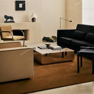 Puede incluir: Una sala de estar con un sofá negro, dos sillones beige con marcos de metal negro y una mesa de centro cuadrada con acabado de espejo. Un taburete negro pequeño se sitúa cerca sobre una alfombra marrón oscuro. Una escultura de león negro.