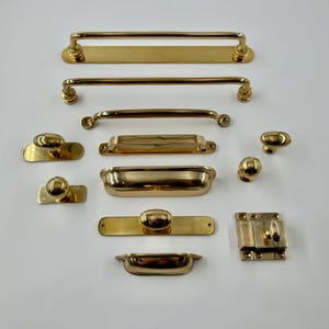 May include: A collection of polished brass hardware including various drawer pulls, cabinet handles, knobs, and a latch. The set features multiple elongated bar handles, recessed cup pulls, oval knobs, and a rectangular latch mechanism with screws.