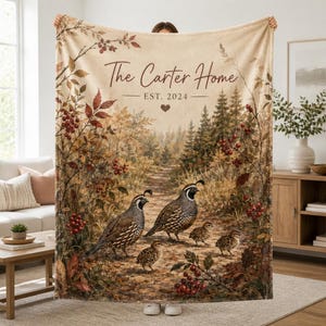 Può includere: Una morbida coperta con una scena di sentiero nel bosco con due quaglie adulte e due pulcini, circondati da fogliame autunnale e bacche rosse. Il testo recita The Carter Home EST. 2024 con una piccola icona a forma di cuore sopra gli uccelli.
