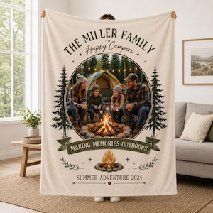 May include: A cream-colored throw blanket featuring a circular photo of a family camping by a fire. Text reads: THE MILLER FAMILY, Happy Campers, MAKING MEMORIES OUTDOORS, and SUMMER ADVENTURE 2024. The design includes pine tree illustrations.