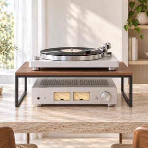 Puede incluir: Un tocadiscos plateado con un disco de vinilo negro se apoya sobre un estante de madera con patas de metal negro. Debajo del estante hay un amplificador de audio plateado con dos medidores VU analógicos con luz amarilla, un mando de volumen y una toma de auriculares.