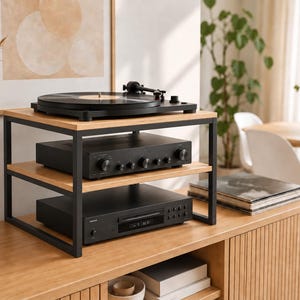 Può includere: Un supporto per apparecchiature audio a due livelli con telaio in metallo nero e ripiani in legno chiaro. Il ripiano superiore ospita un giradischi nero, mentre il ripiano centrale sostiene un amplificatore e quello inferiore un lettore CD.