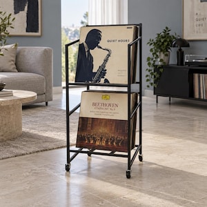 May include: A black metal two-tier vinyl record storage rack on wheels. The top shelf holds a record titled Quiet Hours by Modern Jazz Quartet. The bottom shelf holds a record titled Beethoven Symphony No. 9 by Berlin Philharmonic Orchestra.