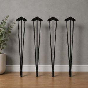 Puede incluir: Un juego de cuatro patas de mueble altas de metal negro, cada una con una placa de montaje triangular en la parte superior y tres varillas delgadas que convergen hacia un pie cilíndrico en la base, ofreciendo un soporte firme.