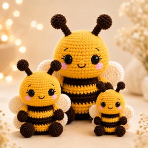 Può includere: Tre peluche a forma di ape realizzati all'uncinetto di diverse dimensioni, ognuno con un corpo a righe gialle e marrone scuro, ali bianche, antenne marrone scuro con punte rotonde, occhi neri, un piccolo sorriso e guance rosa.