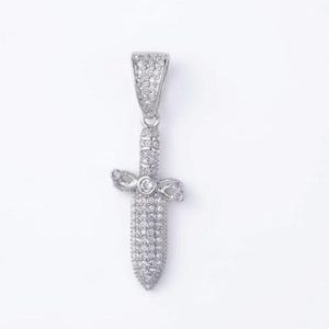 May include: A silver-toned dagger pendant completely encrusted with small, clear, sparkling stones. The piece features a pointed blade, a crossguard with rounded ends, and a large, tapered bail at the top, all covered in pavé-set crystals.