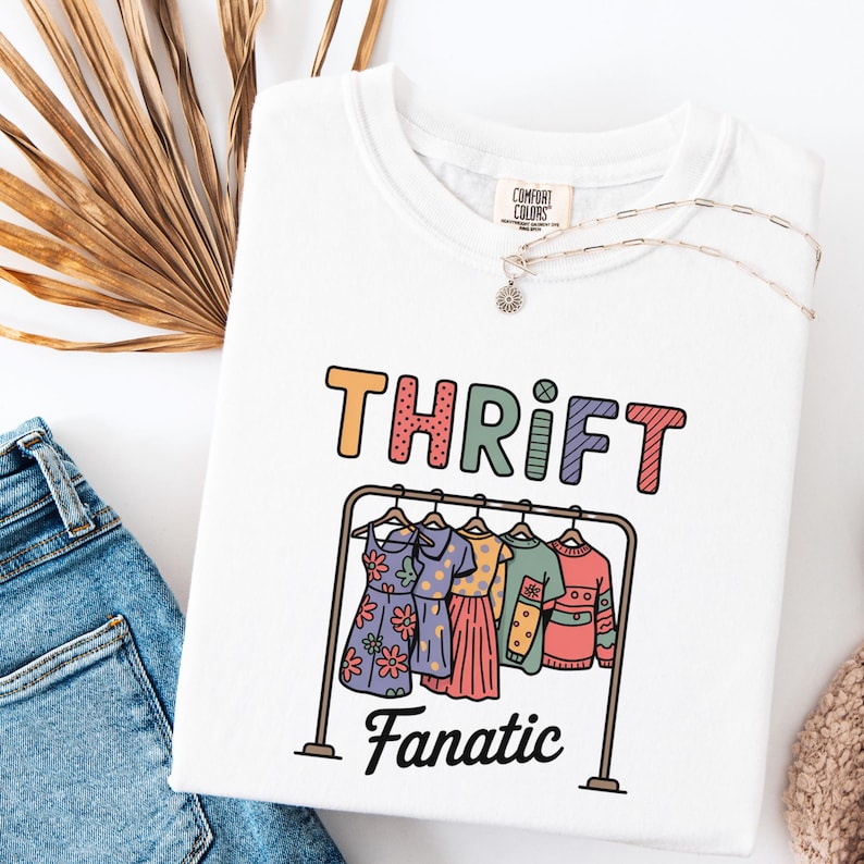 May include: White sweatshirt with the words "THRIFT Fanatic" in colorful letters. Below the text is a graphic of a clothing rack with dresses and sweaters. The sweatshirt has a Comfort Colors tag.