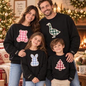 Puede incluir: Cuatro sudaderas negras de cuello redondo con aplicaciones de tela de cuadros vichy. Los diseños incluyen un oso de peluche rosa, un ganso verde, un conejo azul y un árbol de Navidad rojo. Cada puño está bordado con un nombre y un corazón.