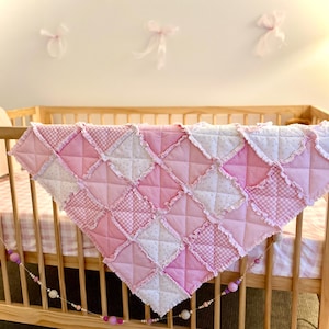 May include: A square rag quilt featuring a patchwork design of pink and white fabric squares. The quilt displays various patterns including gingham, polka dots, and solid pink, with frayed, exposed seams creating a textured, ruffled grid effect.
