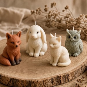May include: A set of four animal-shaped candles including a brown fox, a white rabbit, a white cat, and a grey owl. Each candle features a single white wick at the top. The candles are arranged on a circular wooden slice with a natural grain texture.