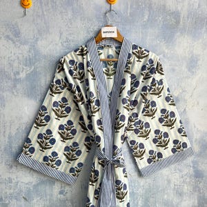 May include: A long-sleeved robe featuring a white background with vertical light blue stripes and a repeating pattern of dark green stems with blue flowers. The garment includes a matching tie belt and blue and white striped trim on the collar.